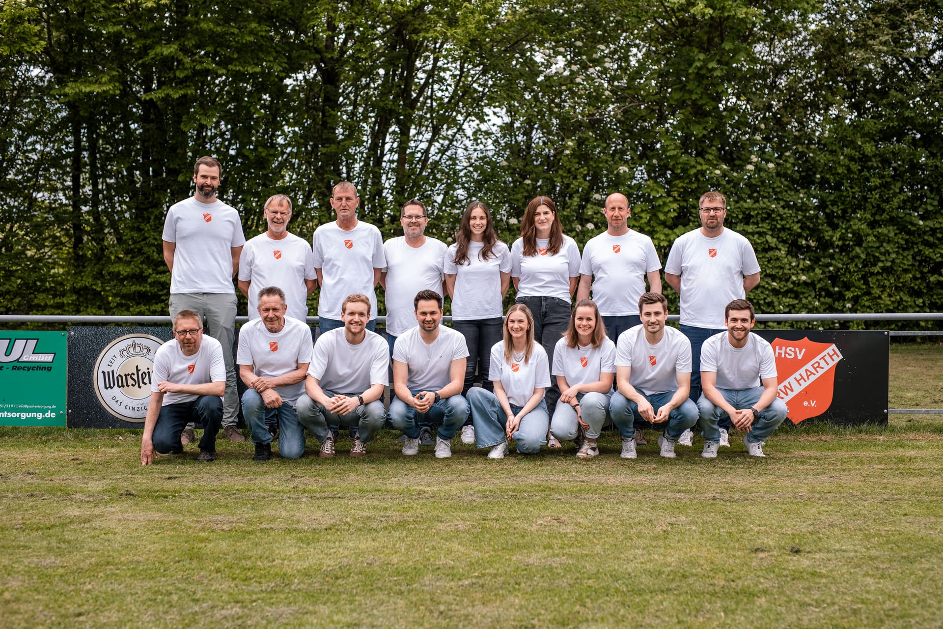 Der Vorstand in weißen Vereins-T-Shirts mit Wappen, in zwei Reihen auf dem Rasen vor der Bande des Sportplatzes